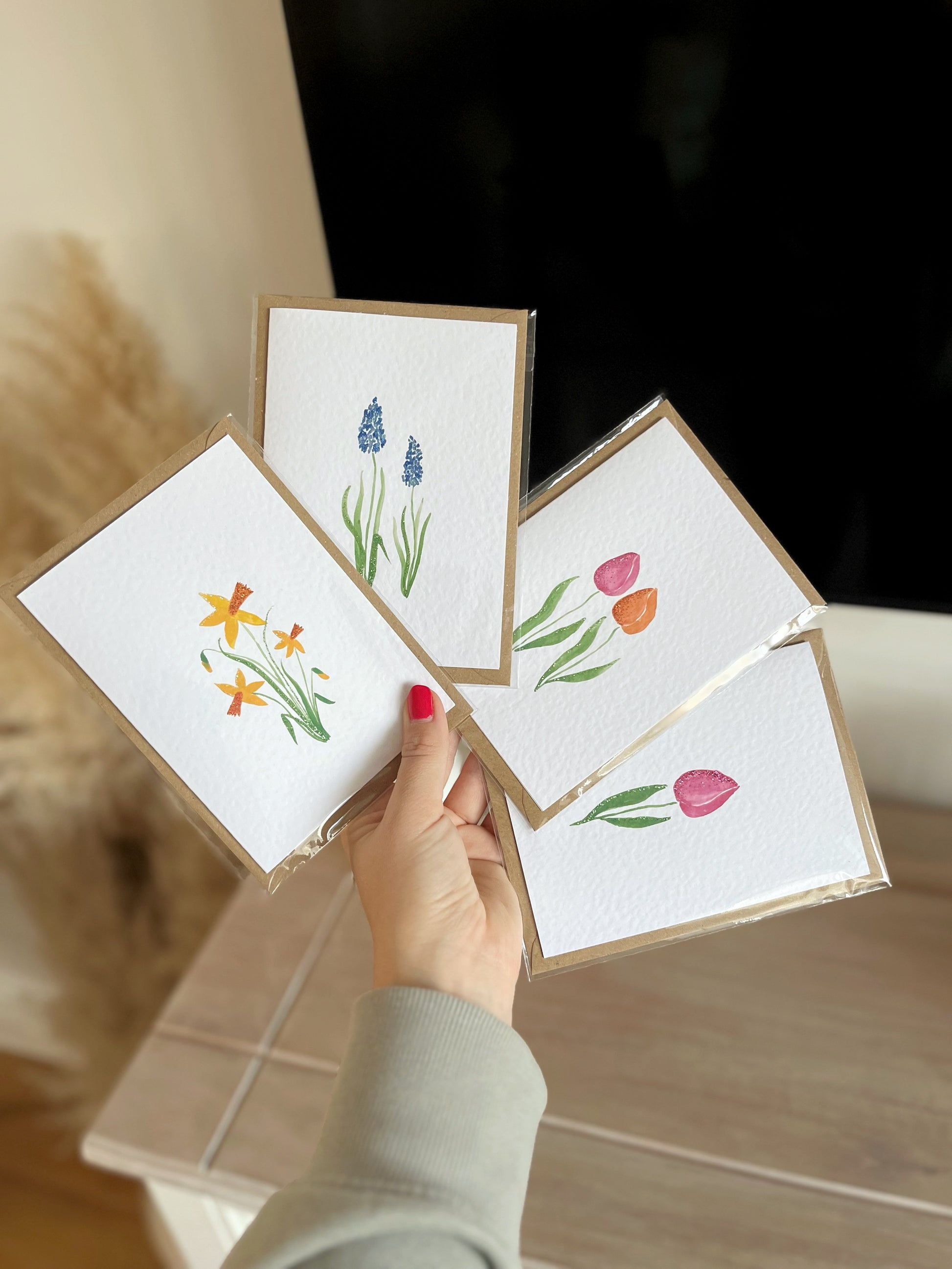 A set of 4 glittery cards including hand painted watercolour illustrations such as daffodils, tulips, a single tulip and muscari. 